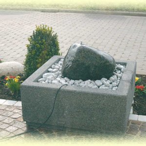 Dunkler       Granit- Quellstein auf hellgrauem Zierkies in Basalt-Becken (Größe       80/80/35 cm)